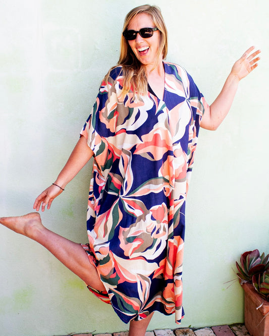 Woman wearing GLORIA Dress with vibrant floral print, enjoying a sunny day outdoors, radiating joy and elegance.