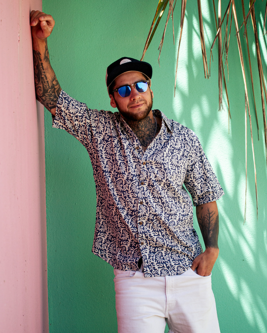 Man wearing a patterned shirt and sunglasses against a green wall with pink corner.