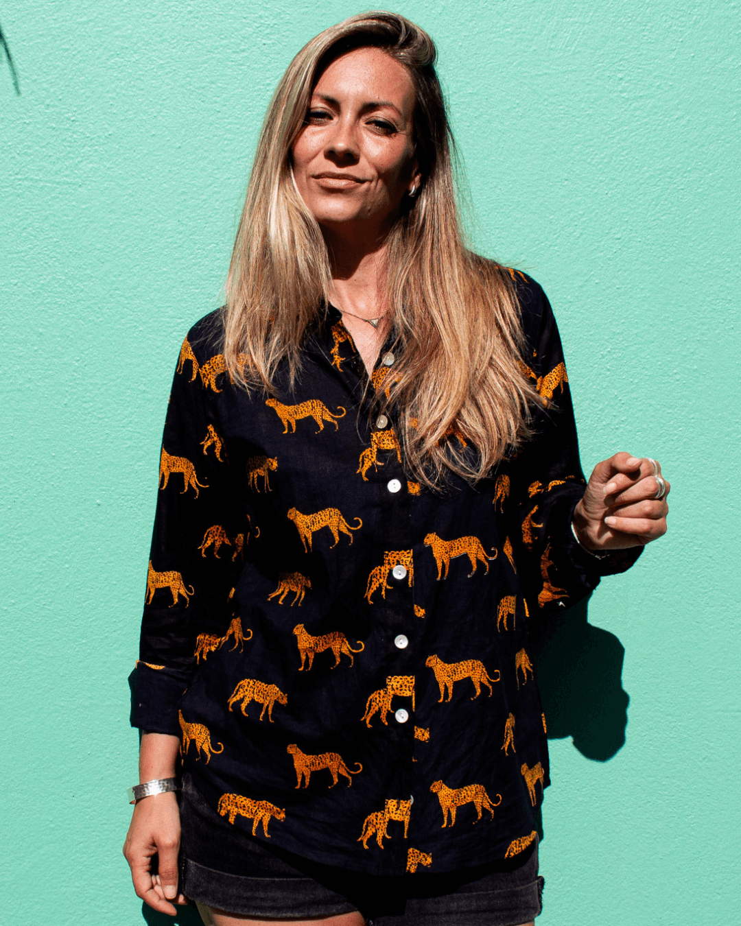LEOPARD Cotton Shirt modeled by a woman, featuring a vibrant leopard print design against a teal background.