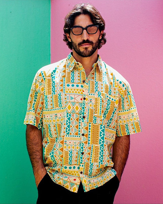 The Cocoon Way short sleeve button down shirt with yellow, white, and turquoise geometric print on a bearded man.