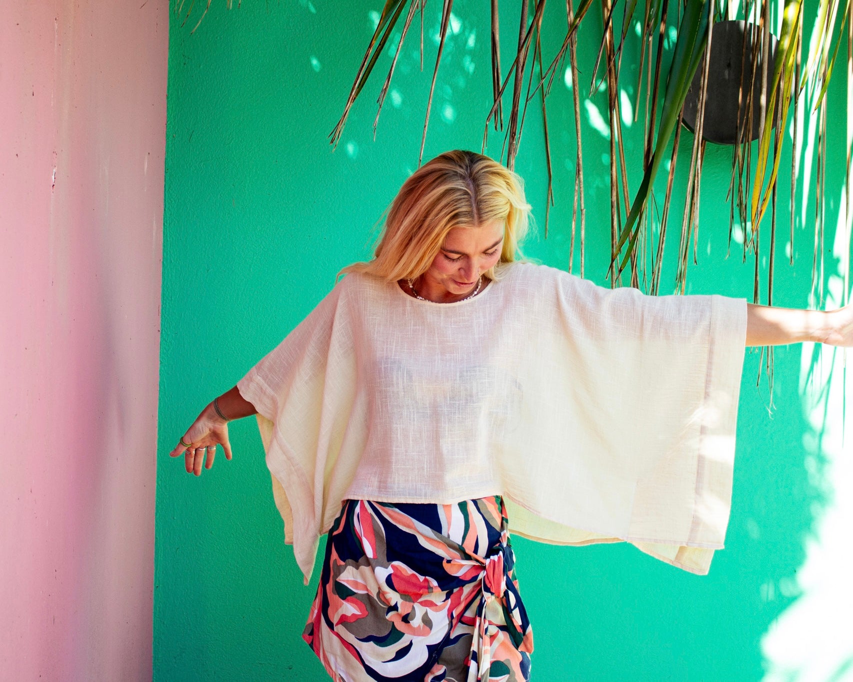Woman wearing the cream ARYA boxy cotton top with batwing sleeves and a floral wrap skirt, The Cocoon Way