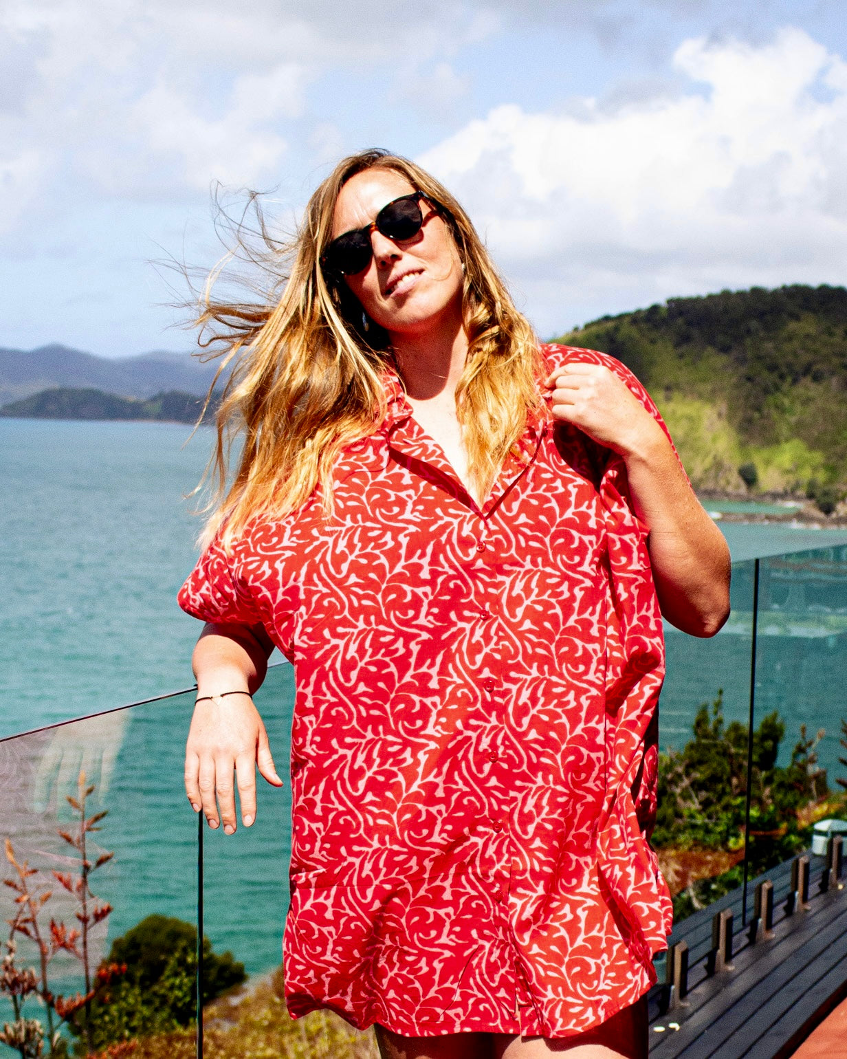 Model wearing ALBA Maxi Shirt in Berry Bloom by the seaside with sunglasses and flowing hair.