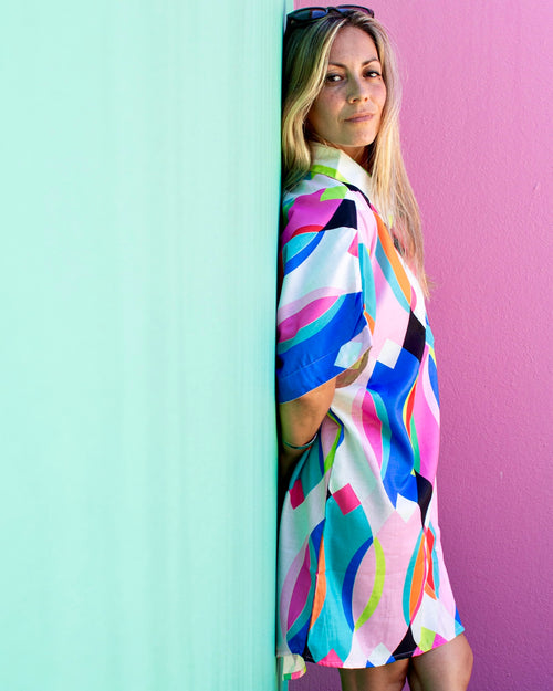 Model wearing the ALBA Maxi Shirt in colorful patterns against a vibrant wall.