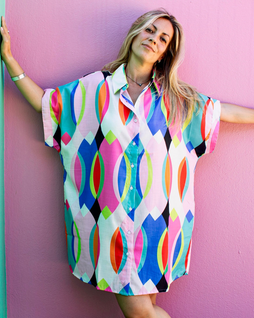 Woman wearing the ALBA Maxi Shirt in a colorful geometric pattern, posing against a pink wall.