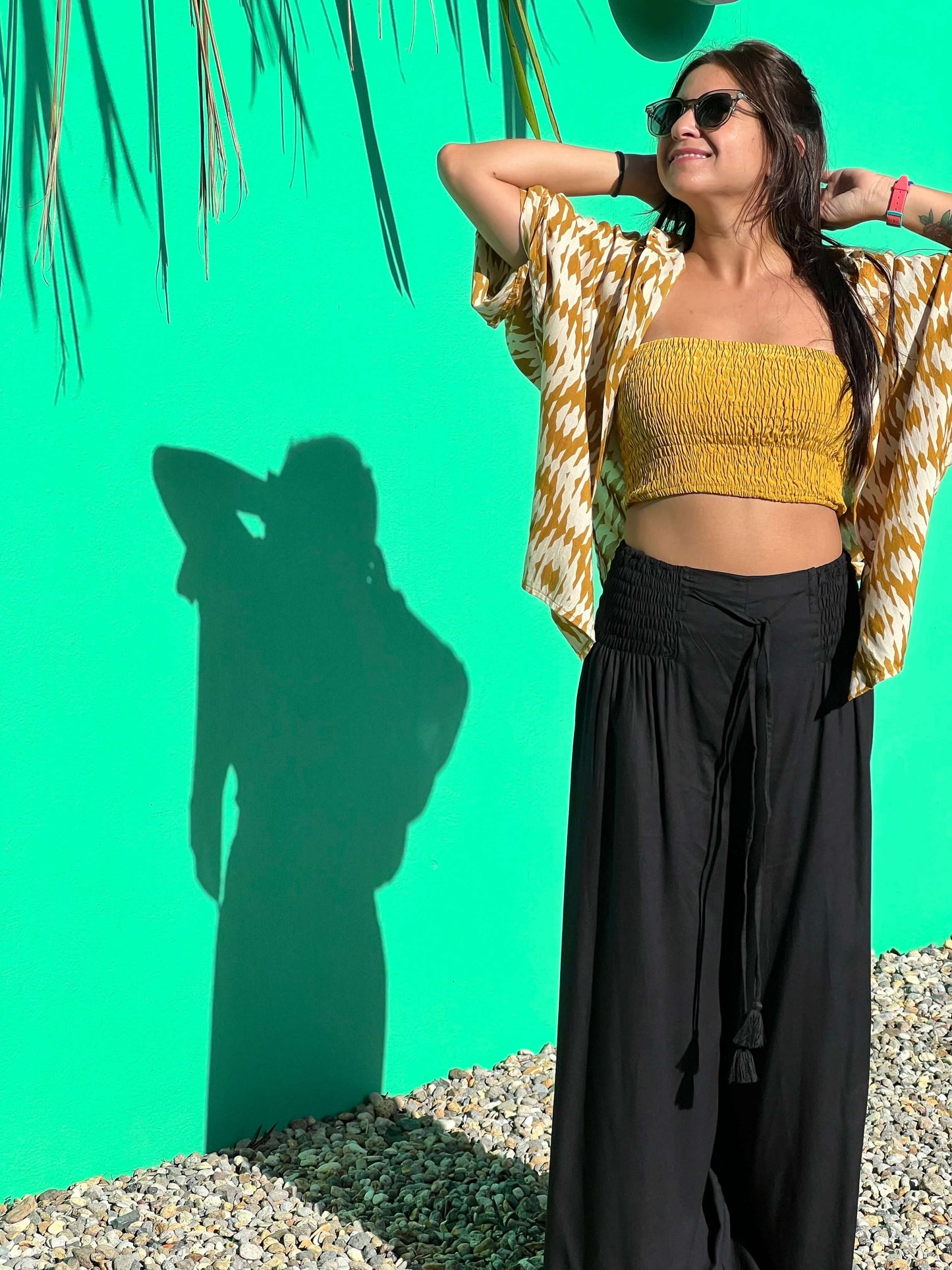 Woman wearing a yellow top and RASA Pants, posing against a vibrant green wall — The Cocoon Way