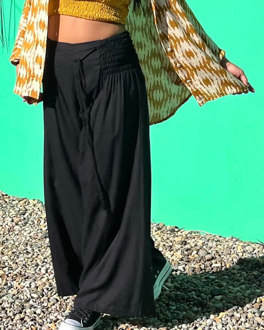 Model wearing RASA Pants Classic Black, showcasing relaxed fit and comfort with a stylish top against a vibrant background — The Cocoon Way