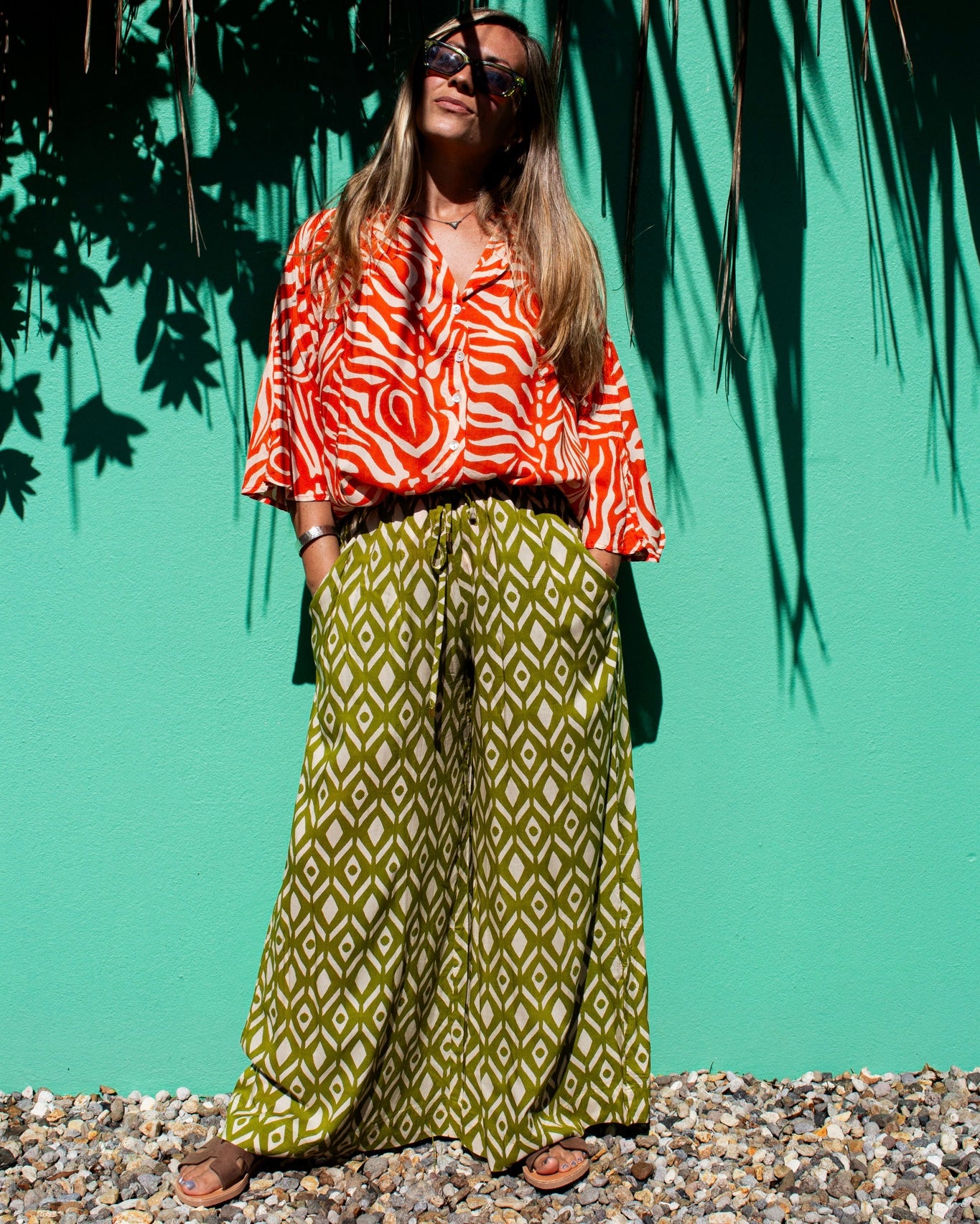 Model wearing OLIVIA Pants in lime ikat pattern with a stylish top and sunglasses against a vibrant green background — The Cocoon Way