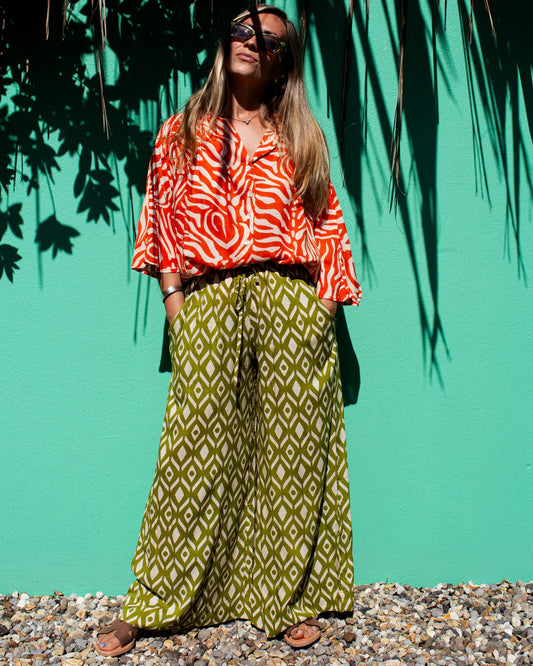 Model wearing OLIVIA Pants in lime ikat pattern with a stylish top and sunglasses against a vibrant green background — The Cocoon Way