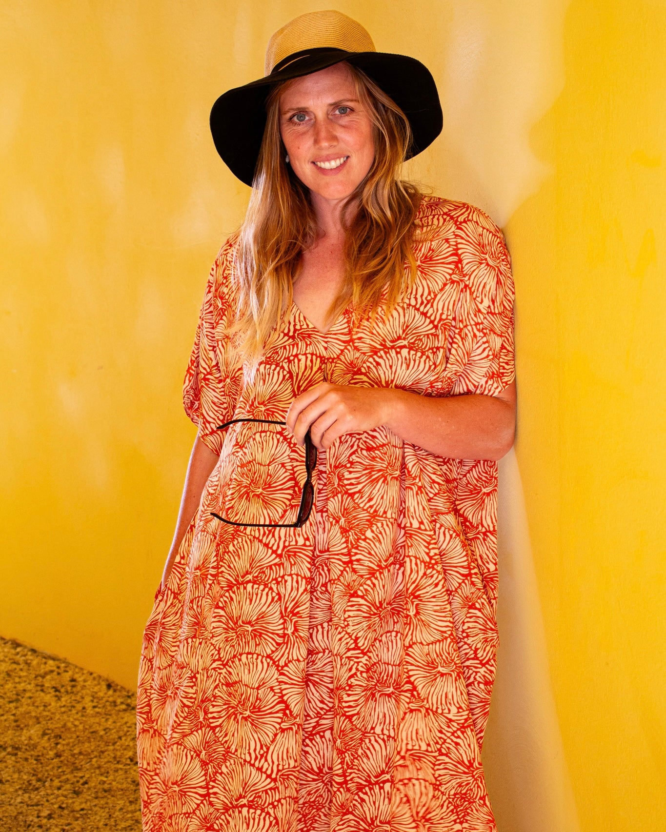 Model wearing GLORIA Dress in Orange Fizz, featuring a flowy kaftan style, set against a vibrant yellow background.