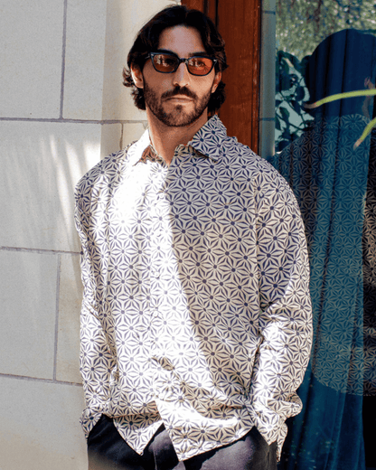 Man wearing SAIRA Long Sleeve Shirt with geometric pattern, standing outdoors with sunglasses.