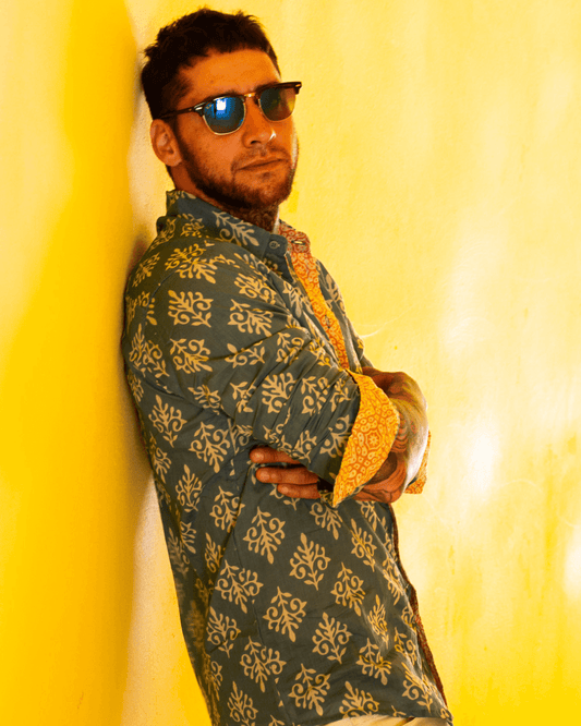 Model wearing the SAIRA Long Sleeve Shirt with sunglasses against a yellow wall, showcasing style and comfort.