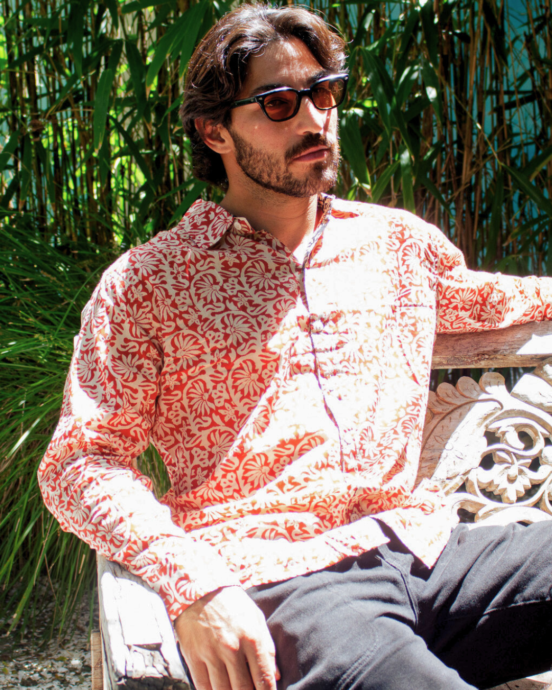 Model wearing SAIRA Long Sleeve Shirt Sevilla in patterned fabric, relaxing outdoors in a lush setting — The Cocoon Way