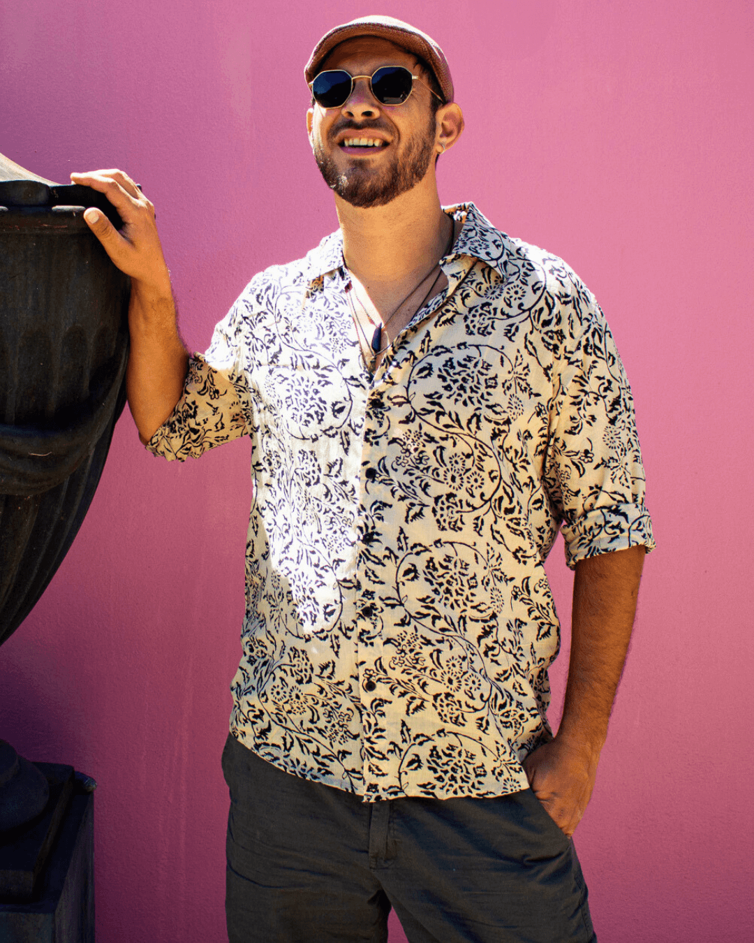 Man wearing a patterned SAIRA long sleeve shirt outdoors with sunglasses, smiling against a colorful background.