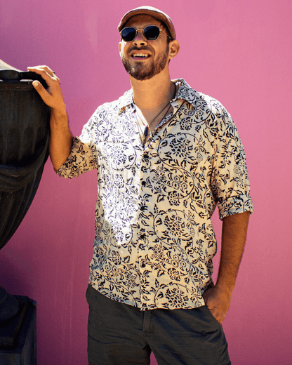 Man wearing a patterned SAIRA long sleeve shirt outdoors with sunglasses, smiling against a colorful background.