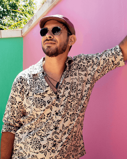 Man wearing a patterned SAIRA long sleeve shirt with sunglasses, posing against a vibrant pink wall.