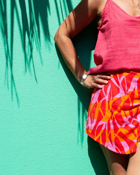 Woman wearing VERA Skort Fuchsia Flame with vibrant colors against a teal wall, showcasing its flowy silhouette — The Cocoon Way