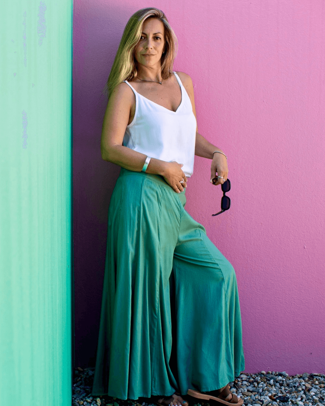 Woman wearing SOFY Pants in teal standing against a pink wall, exuding a stylish, casual vibe.