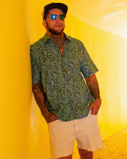 SAIRA Short Sleeve Shirt displayed on a man with tattoos, wearing sunglasses against a bright yellow background.