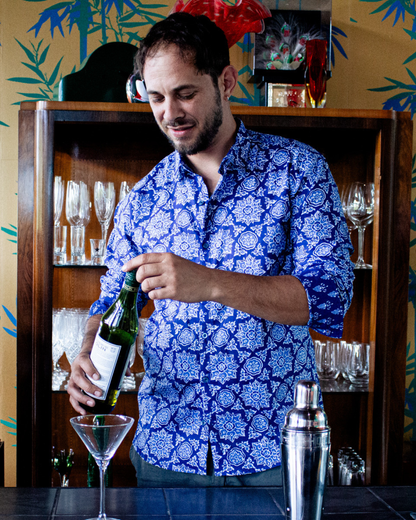 Man wearing a PADMA Long Sleeve Shirt, pouring wine at a bar with glasses in the background.