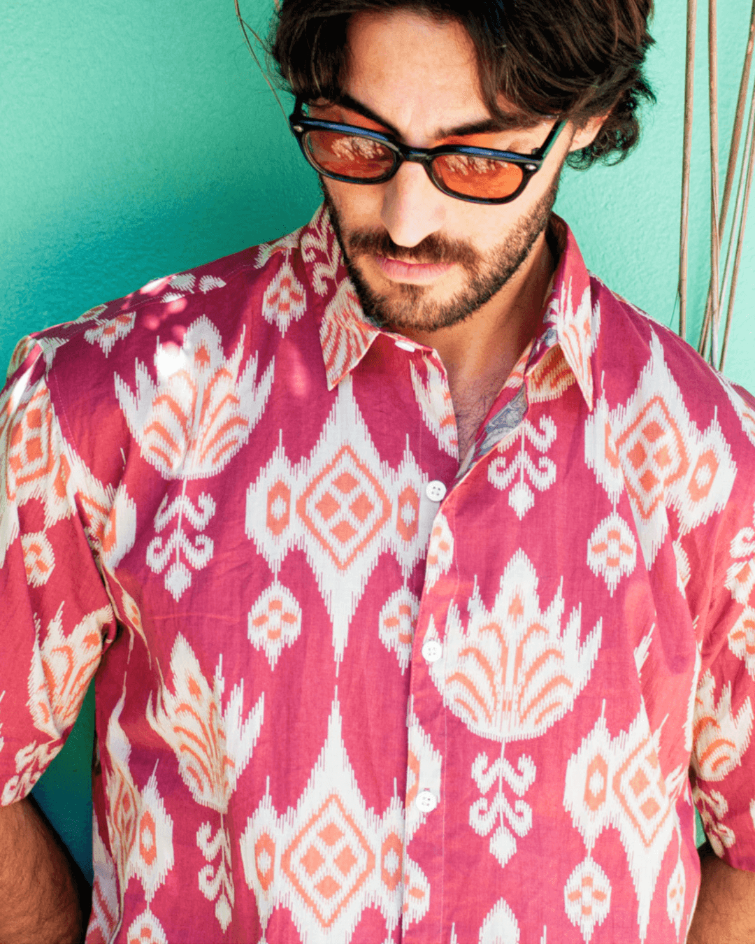 Model wearing PADMA Short Sleeve Shirt Cherry Ikat with vibrant patterns against a colorful background.