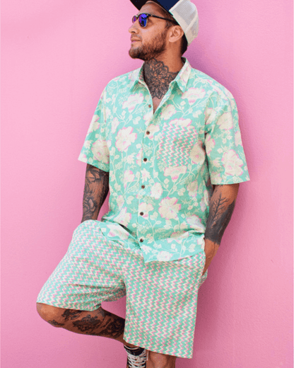 Model wearing a PADMA Short Sleeve Shirt Neon Bloom with tropical patterns against a pink wall.