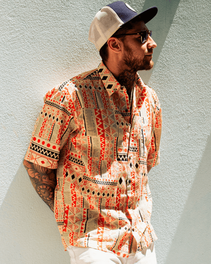 A man wearing a PADMA Short Sleeve Shirt in vibrant orange tribal patterns, showcasing summer style and comfort.