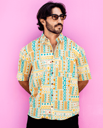 Model wearing PADMA Short Sleeve Shirt in bold yellow tribe print against a pink background.