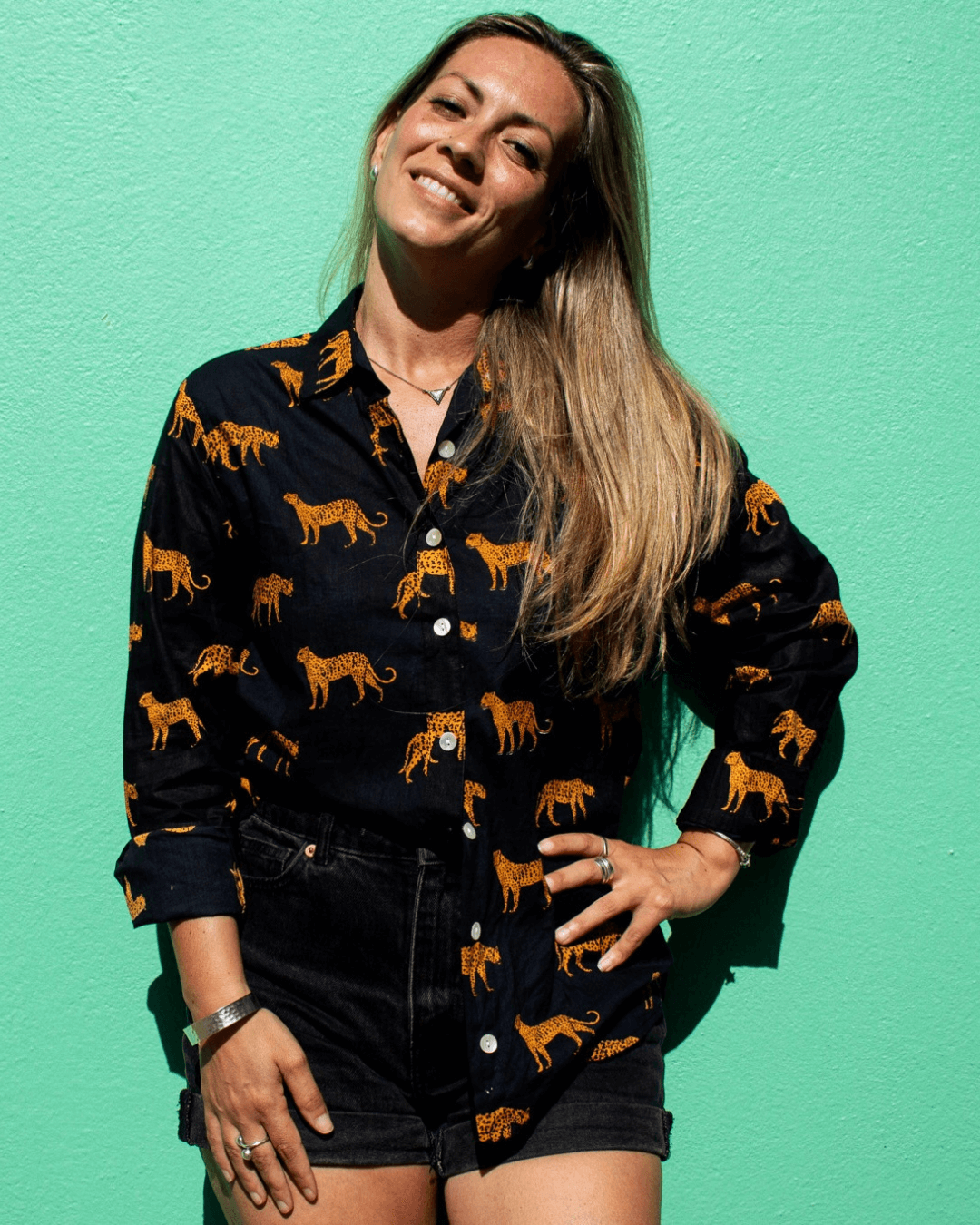 Woman wearing a LEOPARD Cotton Shirt against a vibrant green background, showcasing the shirt's wild charm.