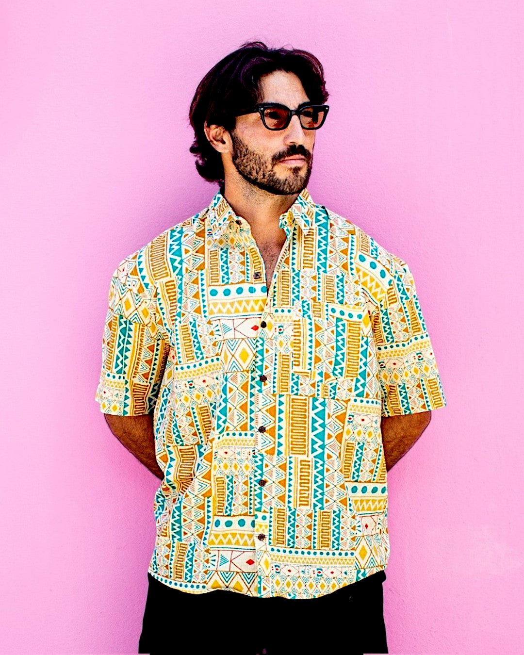 Man wearing The Cocoon Way short sleeve button down shirt with yellow, white, and turquoise geometric print.