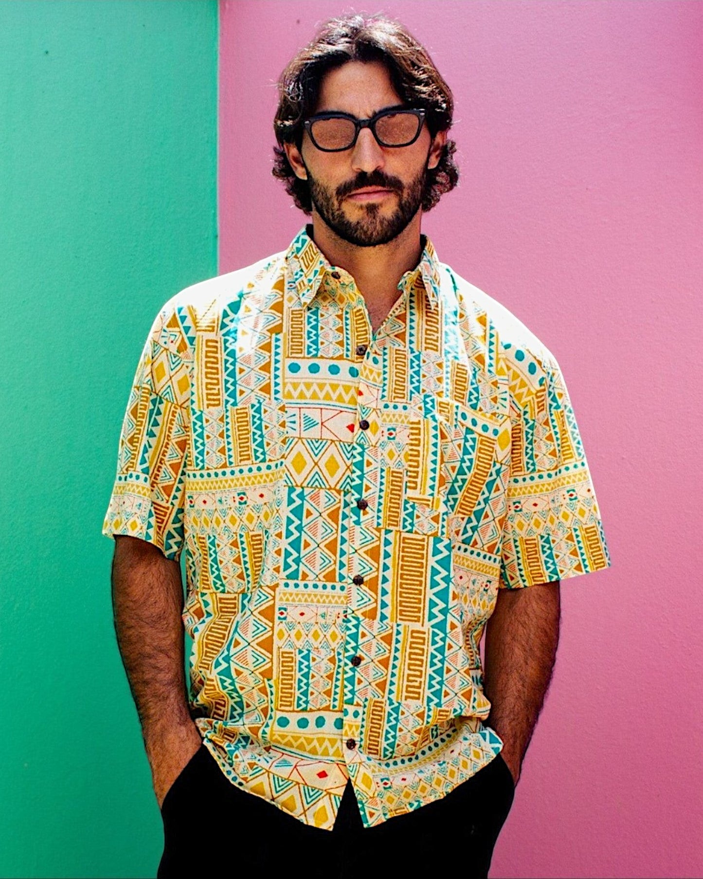 The Cocoon Way short sleeve button down shirt with yellow, white, and turquoise geometric print on a bearded man.